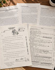 A styled flat-lay of vintage printed documents and letters on aged paper, arranged on a wooden surface with a gold pocket watch, a pen, a book, and a small plant visible around them.
