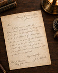 An antique-style handwritten letter on aged beige parchment paper, styled in a vintage desk scene with a brass lamp, magnifying glass, inkwell, thread spool, and old books.